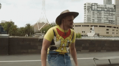 Man In Cowboy Hat And Spongebob Shirt Walking Down Street GIF