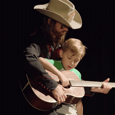 Man In Cowboy Hat Helping Boy Play Guitar GIF