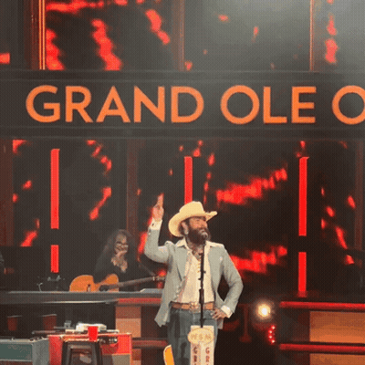 Man In Cowboy Hat On Stage With Grand Oleo Sign GIF