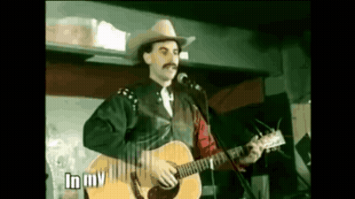 Man In Cowboy Hat Singing Into Microphone Holding Guitar GIF