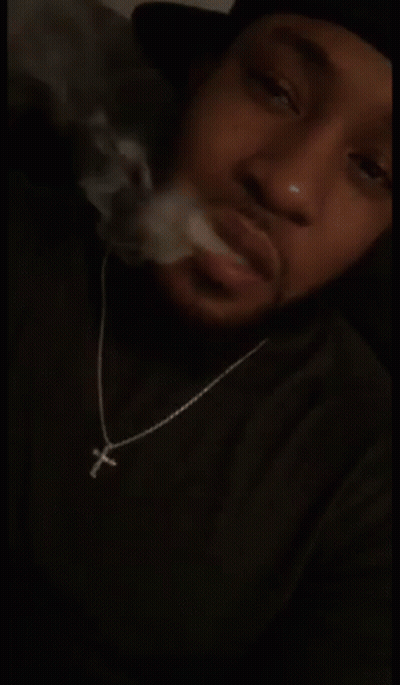 Man In Cross Necklace Smoking In Dark Room GIF