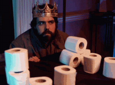 Man In Crown Sits At Table With Toilet Paper Rolls GIF
