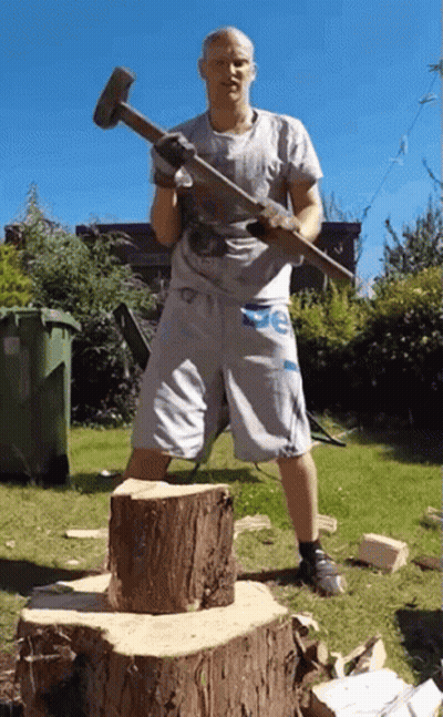 Man In De Shorts Holding Hammer Over Tree Stump GIF