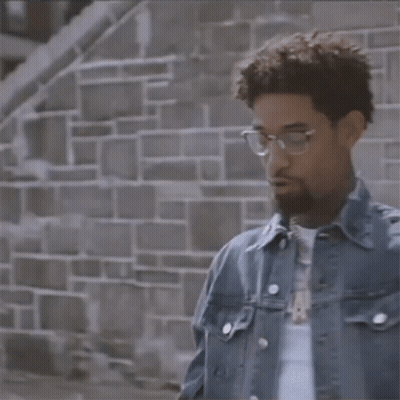 Man In Denim Jacket And Pearl Bracelets In Front Of Brick Wall GIF