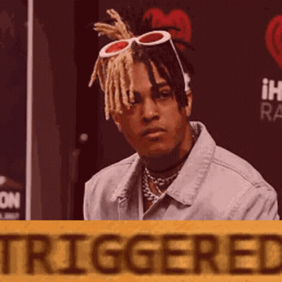 Man In Denim Jacket And Sunglasses Sitting In Front Of Triggered Sign GIF