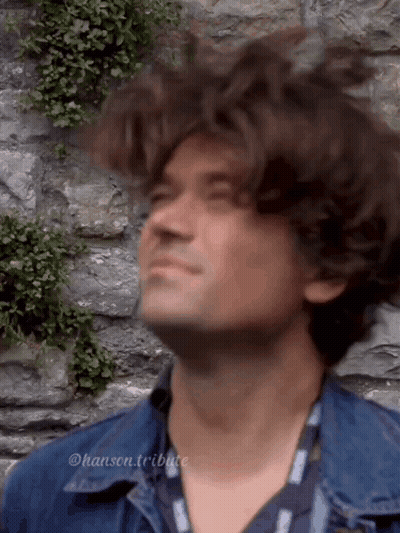 Man In Denim Jacket Looking Up At Stone Wall GIF