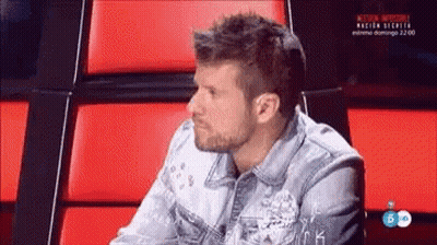 Man In Denim Jacket Sitting In Chair With Red Cushions GIF