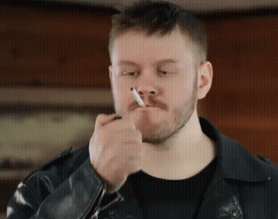 Man In Denim Jacket Smoking Cigarette Under Liberty Jane Sign GIF