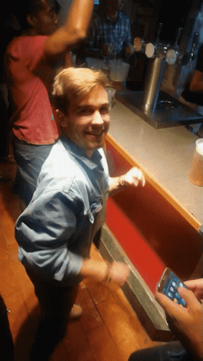 Man In Denim Shirt At Bar With Man In Red Shirt Behind GIF