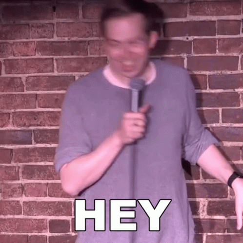 Man In Front Of Brick Wall Holding Microphone Saying Hey GIF