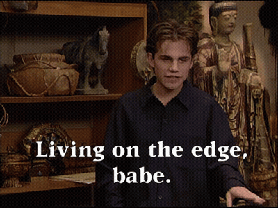 Man In Front Of Shelf With Statue Saying Living On The Edge Babe GIF