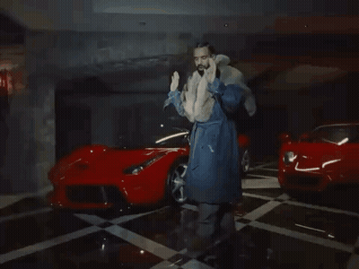 Man In Fur Coat Next To Two Red Sports Cars GIF