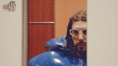Man In Glasses And Blue Jacket In Front Of A & G Wall GIF