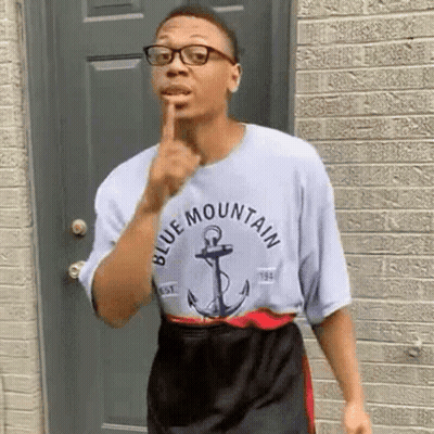 Man In Glasses And Blue Mountain T-Shirt In Front Of Brick Building GIF