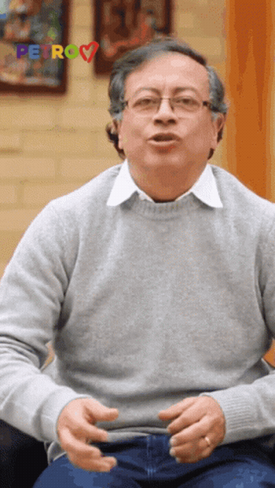 Man In Glasses And Grey Sweater Sitting By Petro Sign GIF
