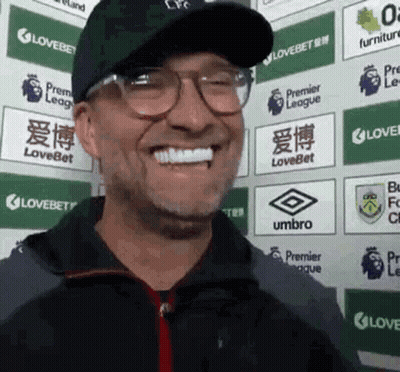 Man In Glasses And Hat Smiling In Front Of Lovebet Signs GIF