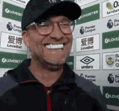 Man In Glasses And Hat Smiling In Front Of Umbro Logos GIF
