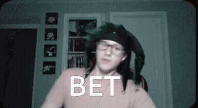 Man In Glasses And Hat Standing Before Bet Wall GIF