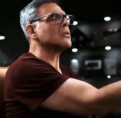 Man In Glasses And Maroon Shirt Sitting In Dark Room GIF