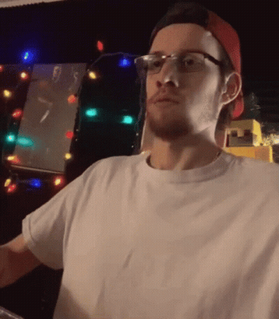 Man In Glasses And Red Hat Standing In Front Of Christmas Tree GIF