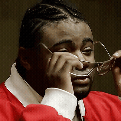 Man in Glasses and Red Jacket Wiping Nose