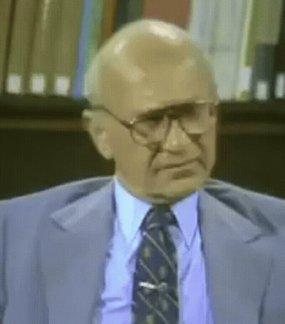 Man In Glasses And Suit Sitting In Front Of Bookshelf GIF