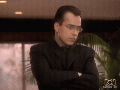 Man In Glasses And Suit With Arms Crossed In Front Of Nuestra Tele Logo GIF
