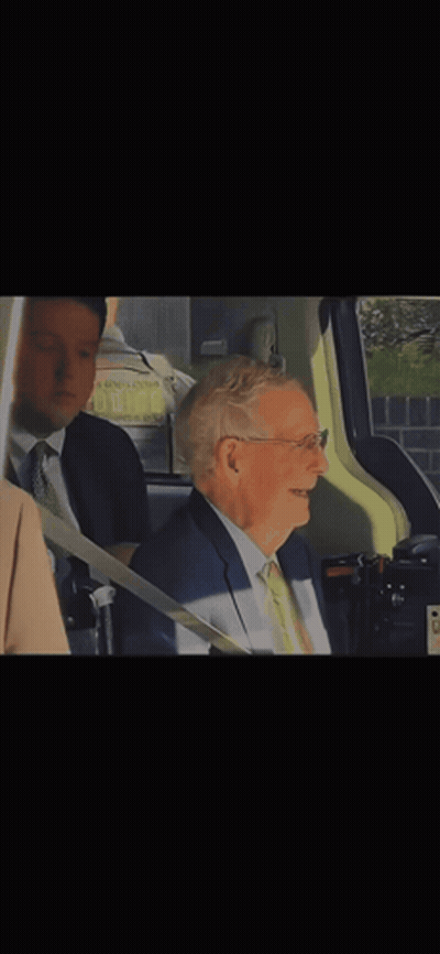 Man In Glasses And Tan Coat Sitting In Blue Chair GIF