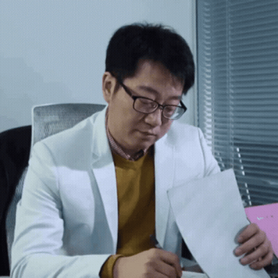 Man In Glasses And White Jacket Holding Paper At Desk GIF
