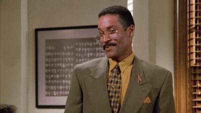 Man In Glasses And Yellow Shirt In Front Of Numbered Picture GIF