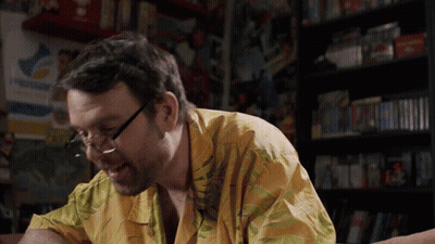 Man In Glasses And Yellow Shirt Sitting In Front Of PlayStation Sign GIF