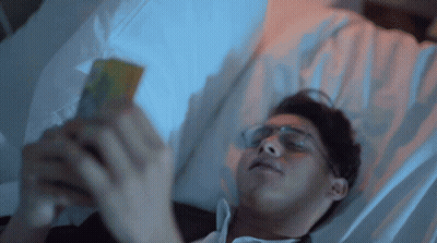 Man In Glasses Laying In Bed On Phone GIF