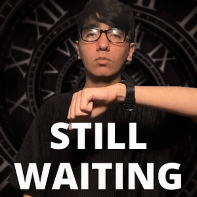 Man In Glasses Standing In Front Of Clock Saying Still Waiting GIF