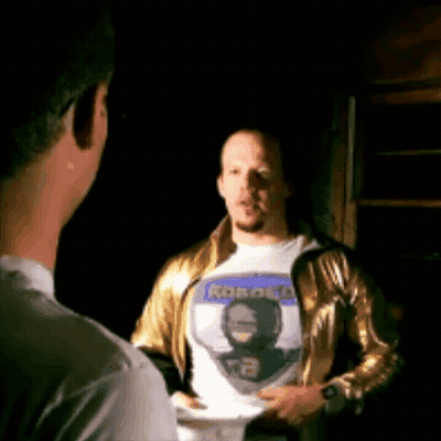 Man In Gold Jacket Talking To Man In Robot T-Shirt GIF