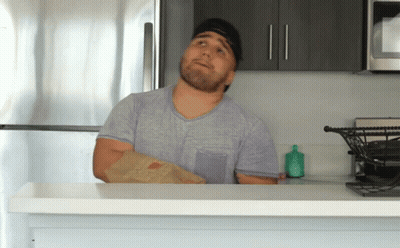 Man In Gray Shirt Holding Bag Of Food In Kitchen GIF