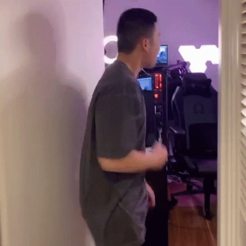 Man In Gray Shirt Standing In Room With Chair And Computer GIF