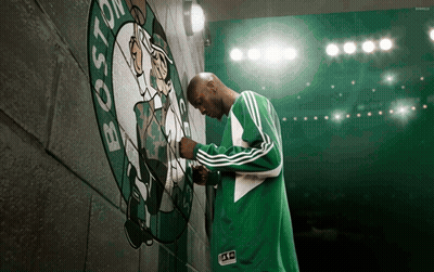 Man In Green Adidas Jacket In Front Of Boston Celtics Logo GIF