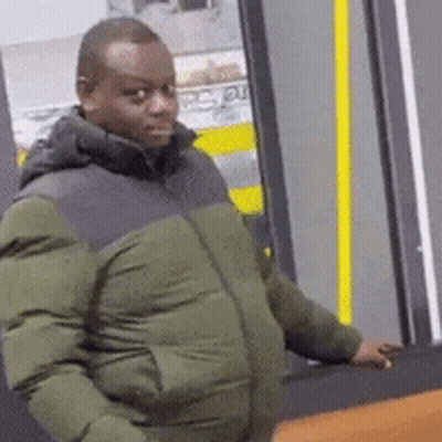 Man In Green And Black Jacket In Front Of Yellow Door GIF