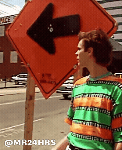 Man In Green And Orange Striped Shirt Beside Arrow Sign GIF