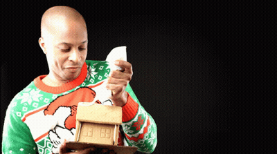 Man In Green And Red Sweater Holding Gingerbread House GIF