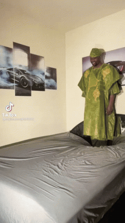 Man In Green Dress Standing On Bed With Cars Wall GIF