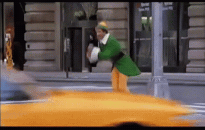 Man In Green Elf Costume Walking Next To Yellow Taxi GIF