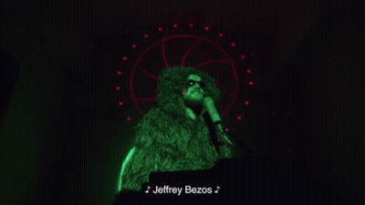Man in Green Fur Coat Singing Into Microphone Jeffrey Bezos