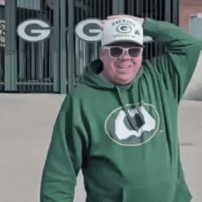 Man In Green Hoodie Sunglasses And Hat In Front Of Green Bay Packers Sign GIF