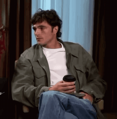 Man In Green Jacket Sitting In Chair Holding Coffee GIF