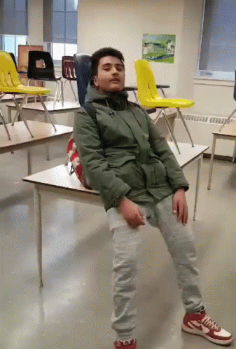 Man In Green Jacket Sitting On Desk In Classroom GIF