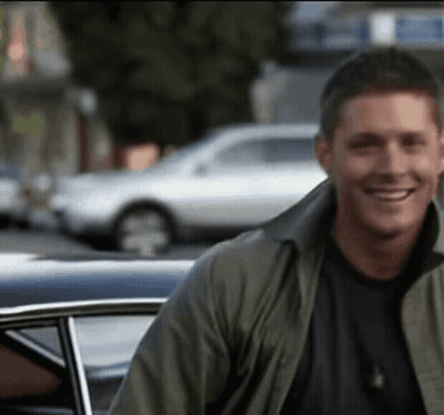 Man in Green Jacket Smiling Next to Car