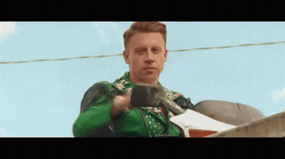 Man In Green Jacket Standing On Roof Holding Cup GIF