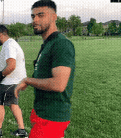 Man In Green Shirt And Red Shorts Next To Man In White Shirt GIF