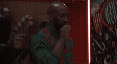 Man In Green Shirt And Red Vest In Front Of Christmas Sign GIF